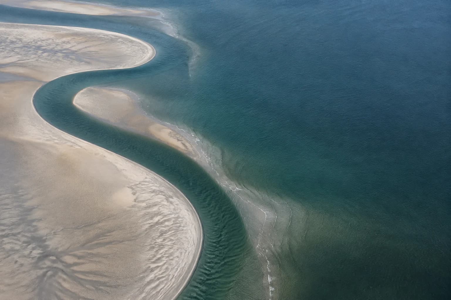 Generierte Luftaufnahme eines geschwungenen Nordseepriels zwischen Sand und petrolblauem Wasser